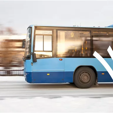 A blue bus is driving on a snow-covered road. The surroundings are wintry and the windows of the bus reflect the light.