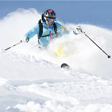 Ein Skifahrer gleitet durch frischen Schnee in den Bergen. Der Himmel ist klar und blau, ideal für einen perfekten Skitag.
