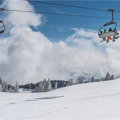 A skier-friendly landscape with snow-covered slopes and a chairlift. The sky is blue and dotted with wispy clouds.