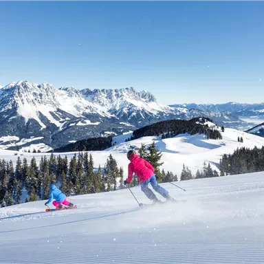 A beautiful winter sports area with snow-covered slopes and mountains in the background. Two skiers enjoy the sun and the fresh air.