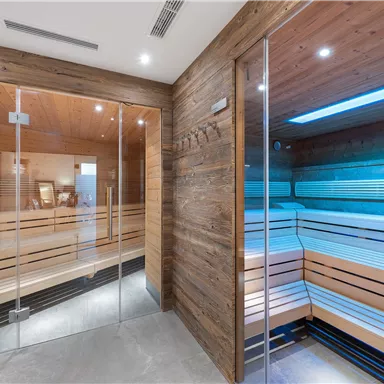Ein moderner Wellnessbereich mit zwei Saunen aus Holz. Die Saunen haben große Glasfenster und sanftes, farbiges Licht.