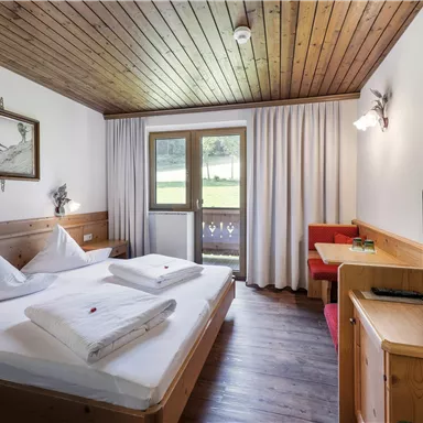 Ein gemütliches Zimmer mit einem Doppelbett und Holzverkleidung. Es gibt einen Balkon, einen Fernseher und eine Sitzecke.
