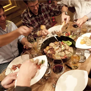 Eine Gruppe von Menschen sitzt an einem Tisch und genießt gemeinsam ein üppiges Essen. Es gibt verschiedene Gerichte und Getränke, während alle miteinander interagieren.
