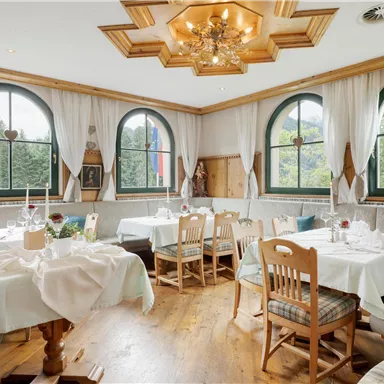 A cozy restaurant with wooden decor and large windows offering views of greenery. Tables are festively set and invite guests to linger.