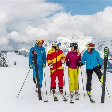 Four skiers are standing on a snow-covered slope with mountains in the background. They are wearing colorful ski clothing and enjoying the winter landscape.