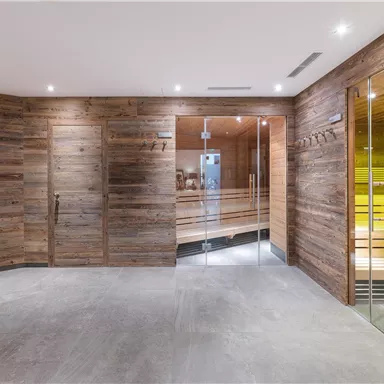 A modern wellness area with wooden paneling and gentle light sources. In the background, a sauna is visible through glass doors.