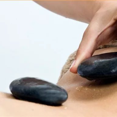 Eine Person erhält eine Heilmassage mit heißen Steinen. Die entspannende Umgebung und die sorgfältige Anwendung fördern das Wohlbefinden.