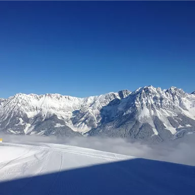 Ein majestätisches Gebirge mit schneebedeckten Spitzen unter einem klaren blauen Himmel. Die verschneite Landschaft strahlt Ruhe und Kälte aus.