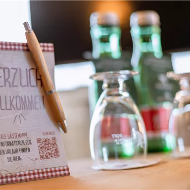 A welcome text on a table with a pen and glasses. Bottles of water are visible in the background.