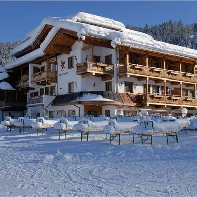 Ein gemütliches Hotel in einer verschneiten Landschaft. Der Schnee liegt auf dem Dach und in der Umgebung, während die Bäume im Hintergrund sichtbar sind.
