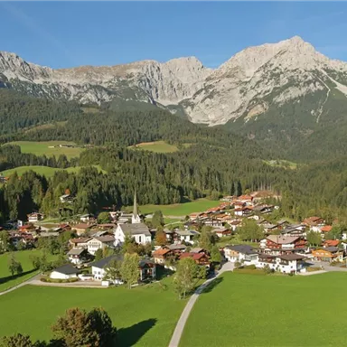 A picturesque mountain landscape with a small town in the valley. The surroundings are green and surrounded by majestic mountains.