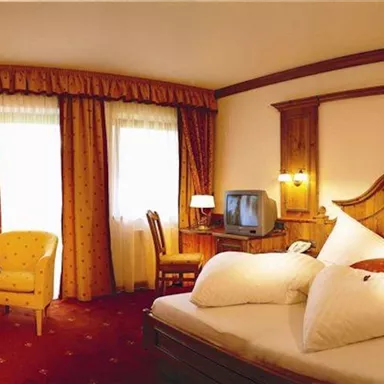 Ein gemütliches Hotelzimmer mit einem Doppelbett und rustikaler Holzgestaltung. Die Fenster lassen viel Licht herein und es gibt einen kleinen Tisch mit Stühlen.