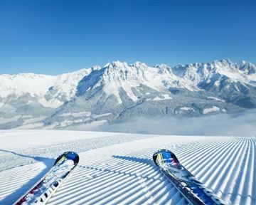 A stunning view of snow-covered mountains and perfect slopes. The sun is shining in the clear blue sky, ideal for skiers.