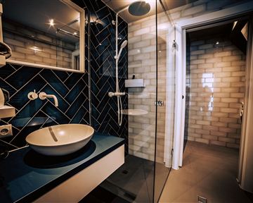 A modern bathroom with blue tiles and an elegant shower. The sink is oval and stylishly placed on a white console.