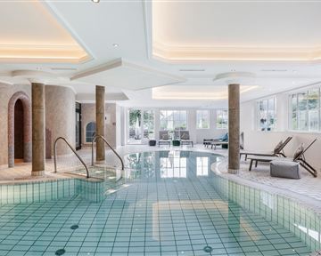 Ein luxuriöser Innenpool mit glattem, grünem Fliesenboden. Die Umgebung ist hell und modern, mit großen Fenstern und bequemen Liegen.
