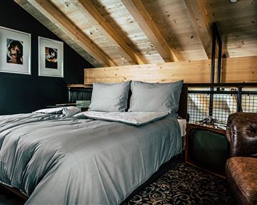 A modern bedroom with a large bed and gray bedding. The wooden beams and the stylish decor create a cozy atmosphere.
