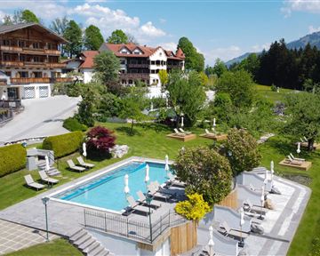A beautiful outdoor area with a pool and loungers. In the background, picturesque mountains and green meadows can be seen.