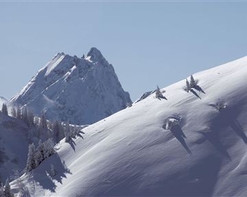 Eine schneebedeckte Berglandschaft mit einem hohen Gipfel im Hintergrund. Der Himmel ist klar und blau, was eine ruhige Atmosphäre schafft.
