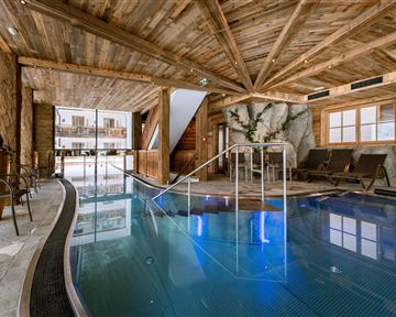 An elegant indoor pool in a wooden building with large windows. Comfortable loungers and natural elements create a relaxing atmosphere.