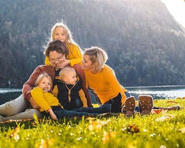 A family is sitting on a meadow by the shore of a lake. They are wearing cheerful yellow clothing and enjoying a sunny day in nature.