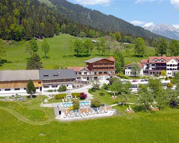 A picturesque hotel in the greenery, surrounded by mountains and meadows. The outdoor area features a pool and well-maintained gardens.