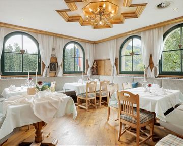 Ein gemütliches Restaurant mit eleganten Tischen und Stühlen. Grote Fenster bieten einen schönen Blick auf die grüne Umgebung.