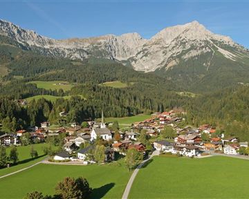 Eine malerische Berglandschaft mit einer kleinen Stadt im Tal. Die Umgebung ist grün und von majestätischen Bergen umgeben.