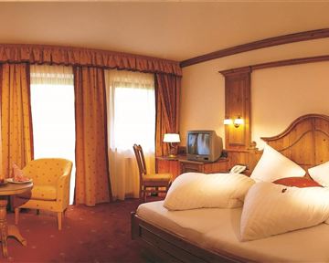 A cozy hotel room with a large bed and colorful curtains. There is a seating area with a table and a television in the room.