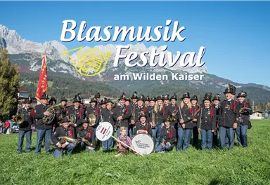 A group of musicians in traditional clothing stands on a meadow. In the background, there are mountains and a clear sky.