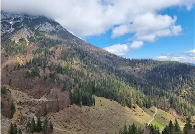 A picturesque mountain landscape with green forests and gentle hills. The sky is partly cloudy and provides a beautiful contrast to nature.