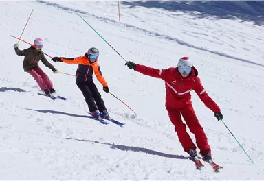 Drei Skifahrer fahren die Piste hinunter. Sie tragen bunte Skikleidung und genießen den Schnee.