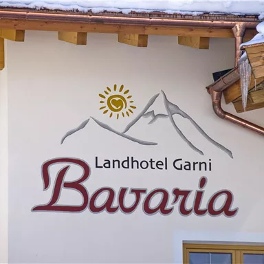 An appealing wall logo of the country hotel Garni "Bavaria" featuring a mountain silhouette and a sun. The warm, inviting design conveys a cozy Alpine atmosphere.