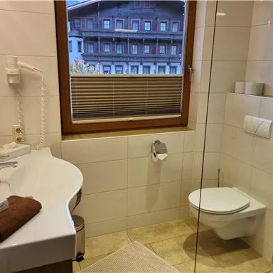 Ein modernes Bad mit einer großen Dusche und einem stilvollen Waschbecken. Durch das Fenster blickt man auf ein Gebäude im alpinen Stil.