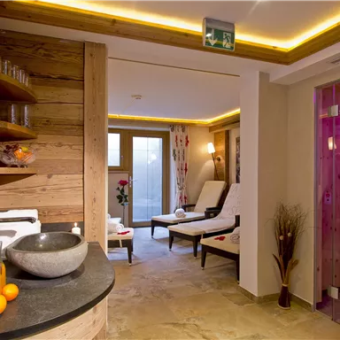 A relaxing spa area with wood paneling and soft lighting. Comfortable loungers and a modern wellness shower invite you to unwind.