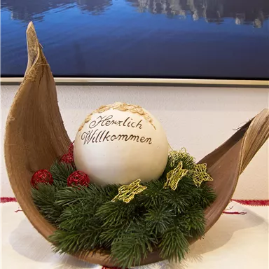 A decorative Christmas arrangement with a large, labeled ball in the center. Surrounded by fir branches and red berries, it radiates a festive atmosphere.