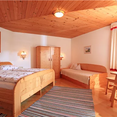 Ein gemütliches Schlafzimmer mit Holzdecken und einem Doppelbett. Das Zimmer ist hell und freundlich, mit einem kleinen Tisch und Stühlen.