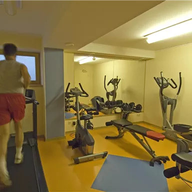 A fitness room with a treadmill and various exercise equipment. A person is jogging on the treadmill.