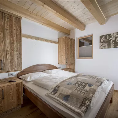 Ein gemütliches Schlafzimmer mit einem großen Bett und Holzregalen. Die Wände sind hell gestrichen und es gibt ein Fenster, das natürliches Licht hereinlässt.