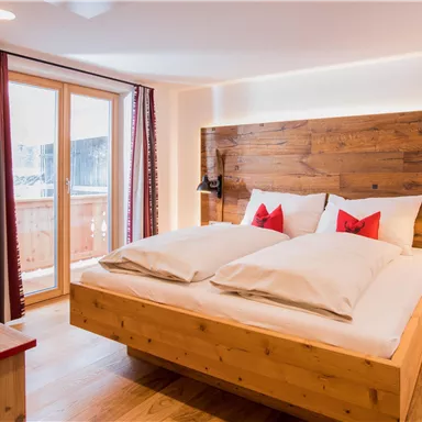 A cozy bedroom with a large bed and wooden details. A lot of daylight comes in through the windows.