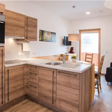 A modern kitchen with wooden cabinets and an elegant design. The room is bright and friendly with a table and chairs.