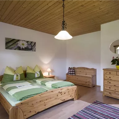 Ein gemütliches Schlafzimmer mit einem großen Doppelbett und hellem Holzmobiliar. Die Wände sind in neutralen Farben gehalten, und es gibt dekorative Elemente wie Lampen und Pflanzen.