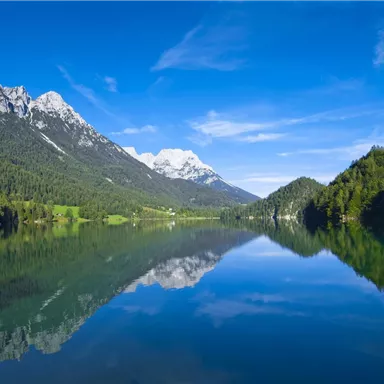 A beautiful lake surrounded by mountains and trees. The clear sky is reflected in the water.