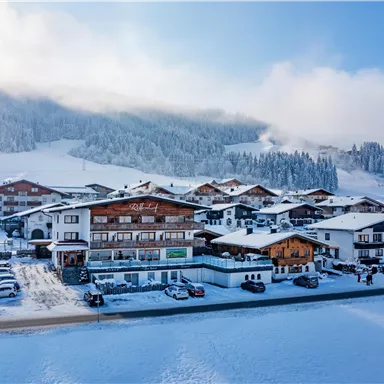 Eine verschneite Landschaft mit traditionellen Chalets und Bergen im Hintergrund. Der Himmel ist klar und die Umgebung wirkt ruhig und einladend.