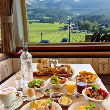 Ein köstliches Frühstück mit verschiedenen Speisen wie Eiern, Brot und Obst. Im Hintergrund ist eine malerische Aussicht auf die Berge und das grüne Tal zu sehen.