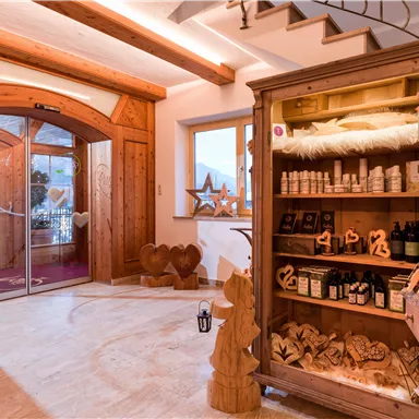 Ein einladender Eingangsbereich mit einer Holzvitrine, die verschiedene Produkte zeigt. Die Türen sind aus Glas und es gibt eine gemütliche Atmosphäre mit dekorativen Holzskulpturen.