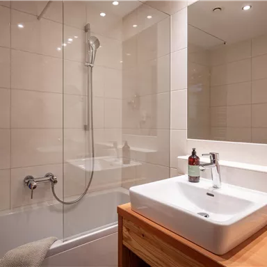 Ein modernes Badezimmer mit einer Dusche und einem eleganten Waschbecken. Die Wände sind in hellen Fliesen gehalten und es gibt einen Holzbereich.