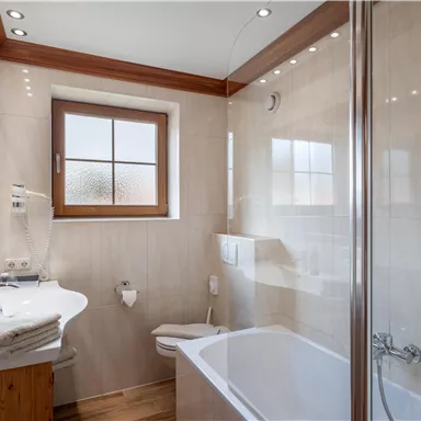 Ein helles Badezimmer mit einer Badewanne und einer Duschkabine. Es hat eine moderne Ausstattung und ein großes Fenster.
