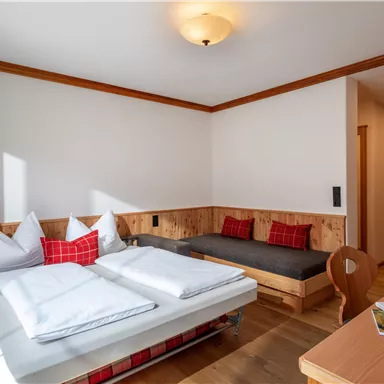 Ein gemütliches Zimmer mit einem Doppelbett und einem Sofa. Die Holzdetails und das helle Licht schaffen eine freundliche Atmosphäre.
