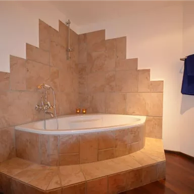 Ein modernes Badezimmer mit einer stilvollen Badewanne und einer interessanten Wandgestaltung. Handtücher in orange und blau ergänzen das Ambiente.