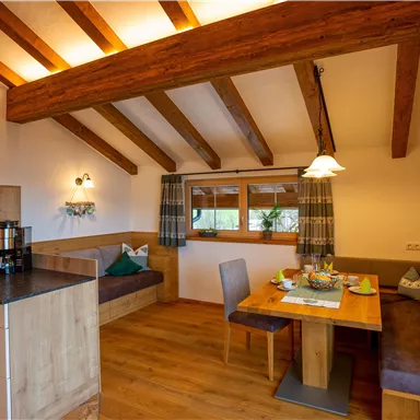 Eine gemütliche Wohnung mit Holzbalkendecke und moderner Kücheneinrichtung. Der Essbereich ist einladend und hell mit einem Blick nach draußen.